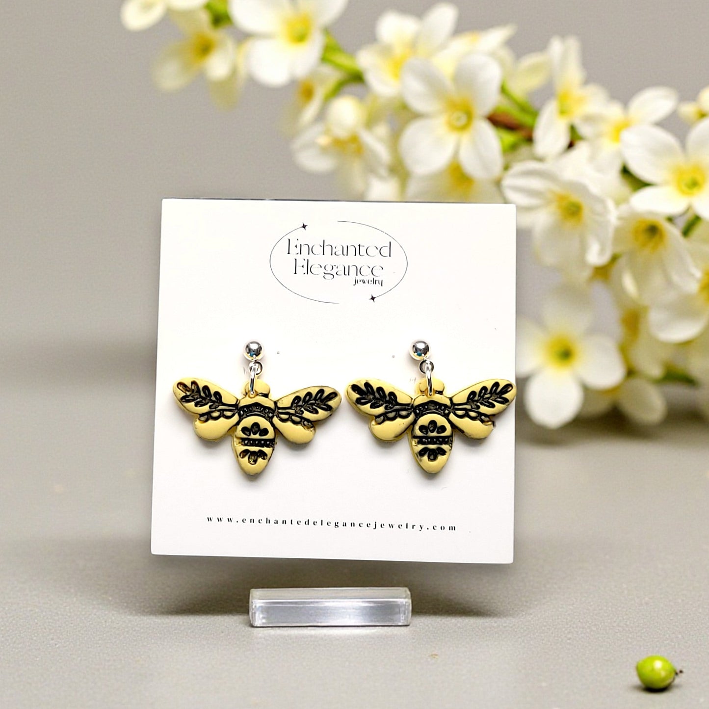 Yellow embossed bee-shaped earrings on a card with white flowers in the background