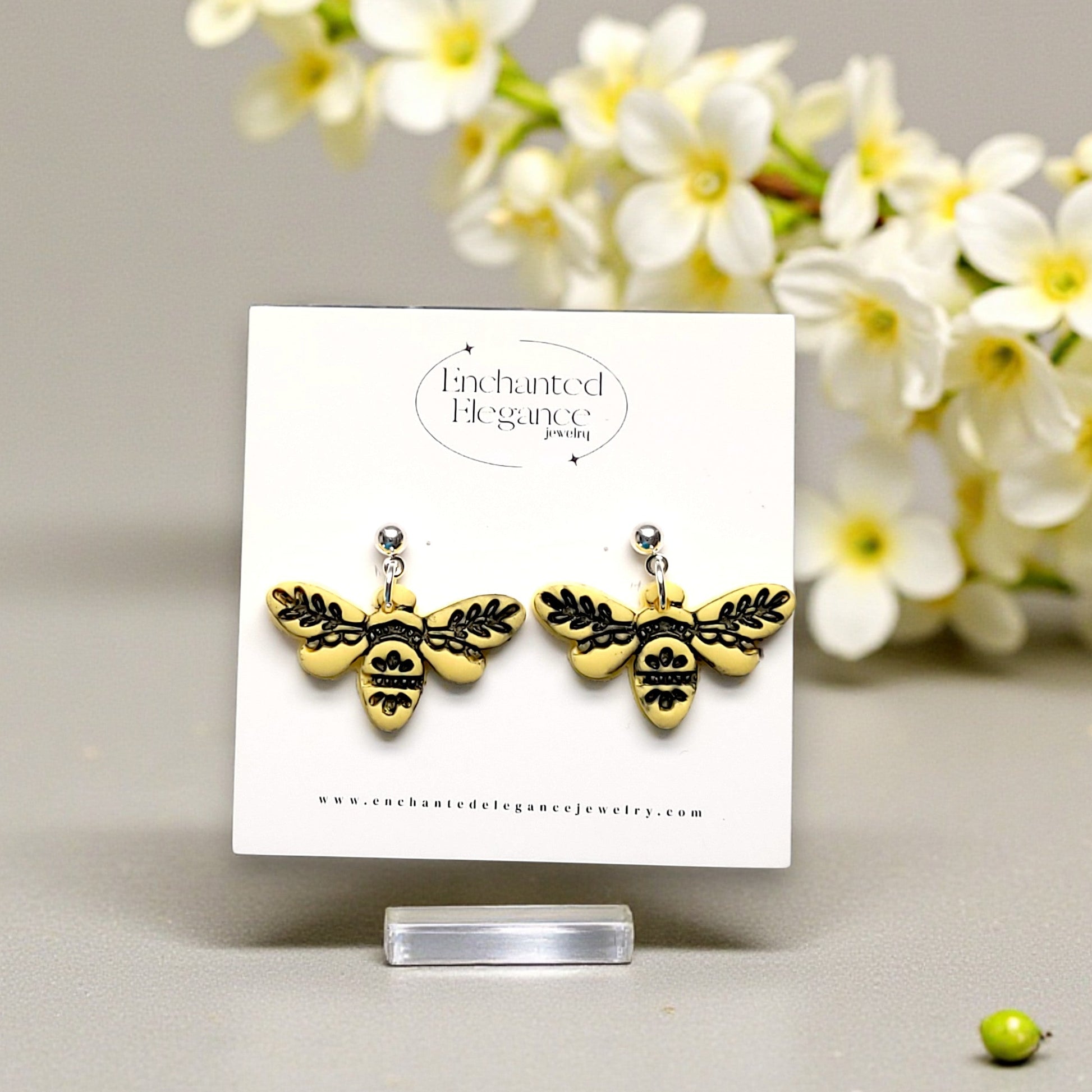Yellow embossed bee-shaped earrings on a card with white flowers in the background