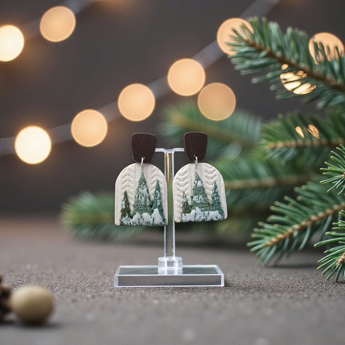 Earrings with a forest design on a stand with Christmas decorations and lights in the background