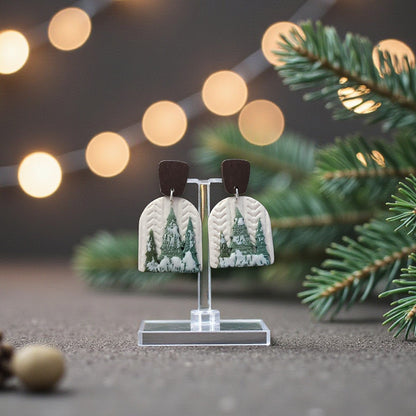 Earrings with a forest design on a stand with Christmas decorations and lights in the background